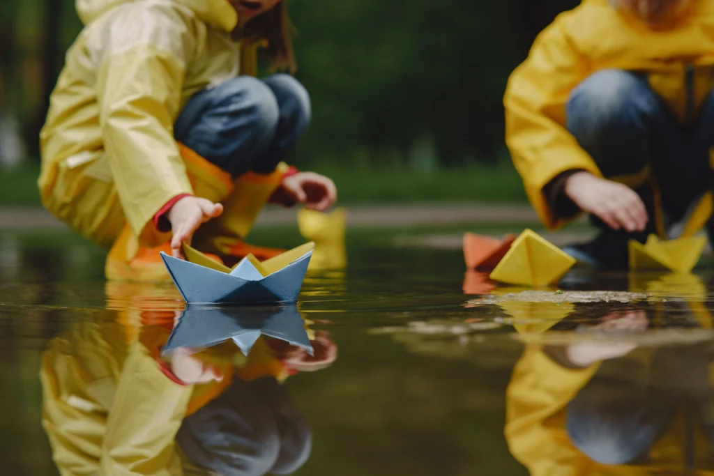 Kids playing with paper boats in rain